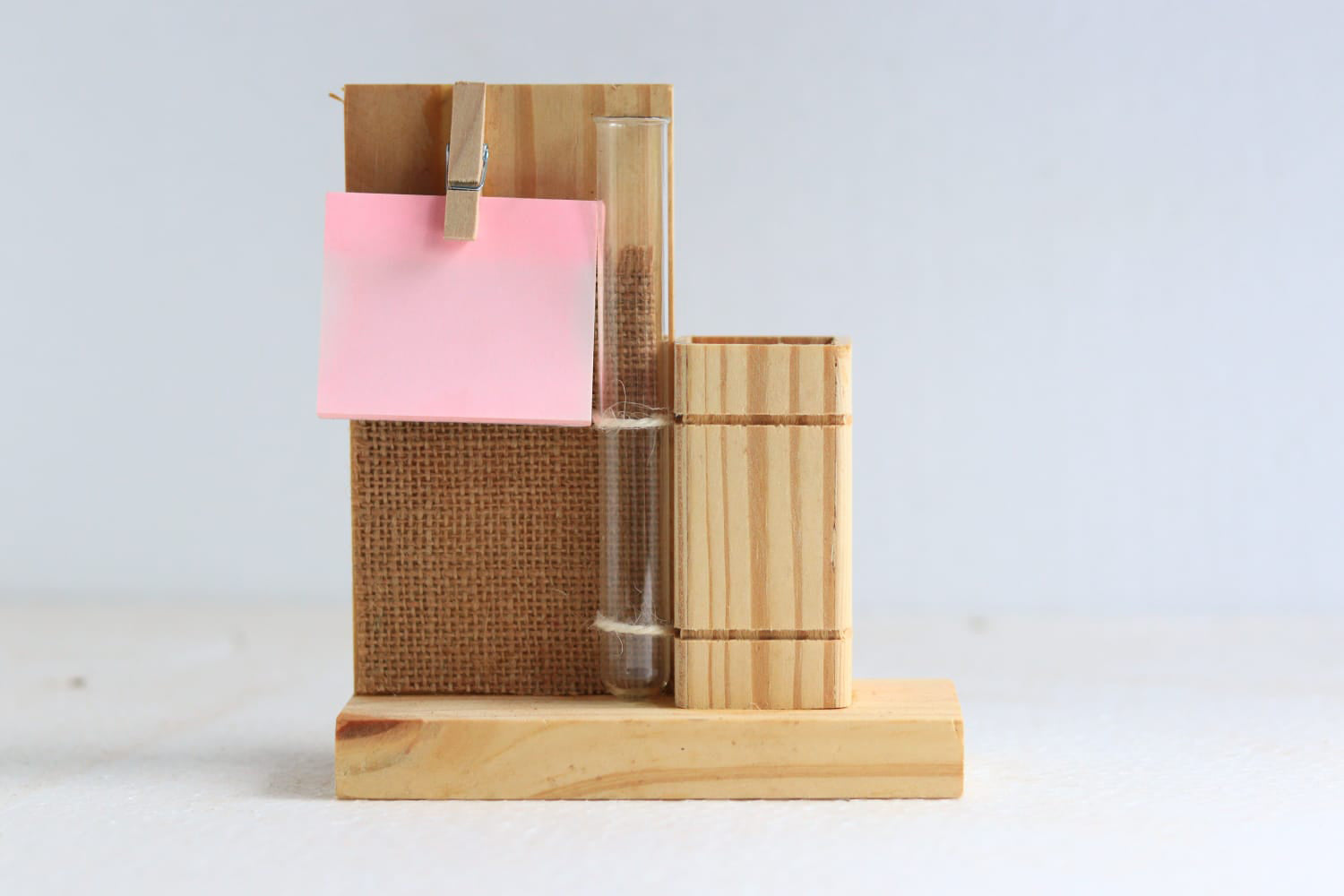 Front view of a wooden pen stand for holding pens and a wooden clip holding notes. A Test tube with attached to the pen holder with 2 strings. 